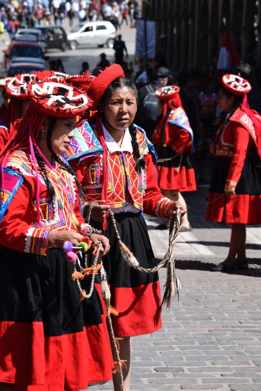 s in red dresses with colorful heads coverings, carrying parasols