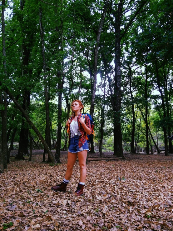 a girl standing among some trees and leaves