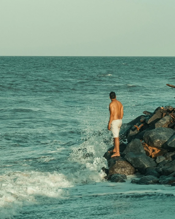 a man walking in the surf near some rocks