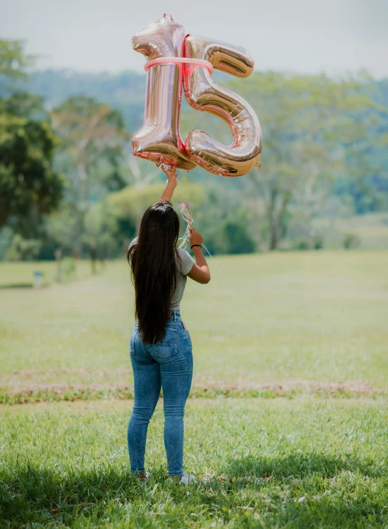 girl standing in the field holding three large balloons to the number twenty five