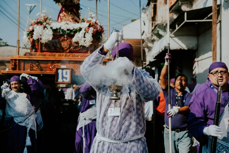 a man wearing a purple robe and holding up a cup in front of a group of people