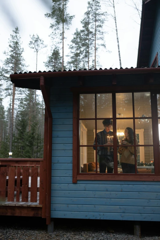 a man and woman stand in the window of a small blue cabin