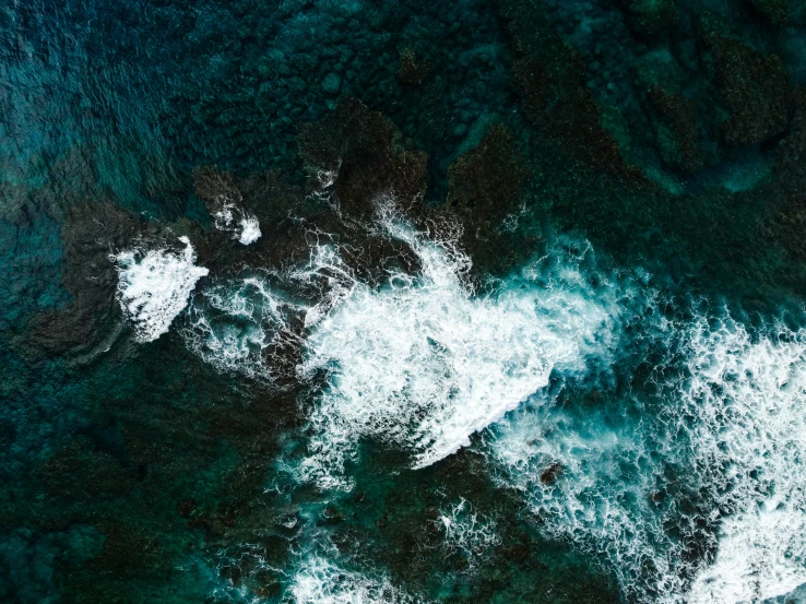 an aerial view of the ocean with rocks and waves