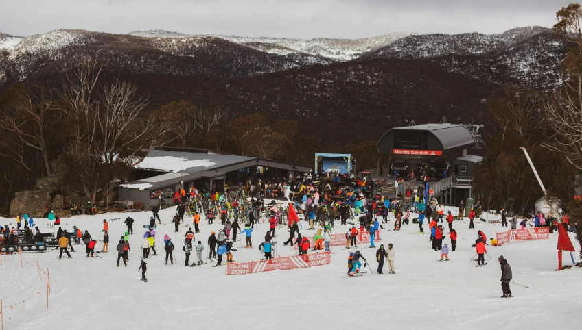 many people are standing on the snow near the ski area