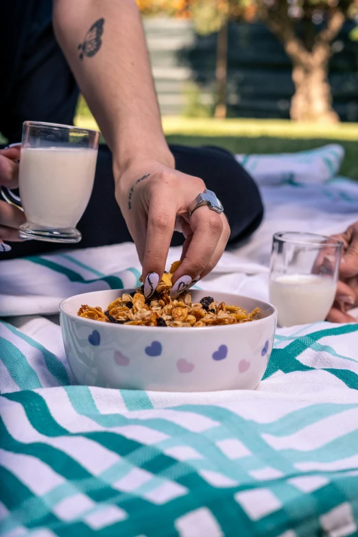 two people eat granola from a bowl on a picnic blanket