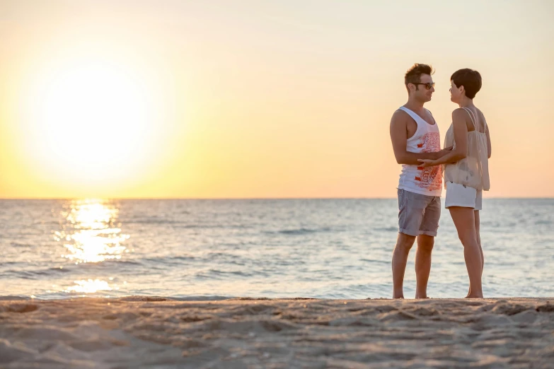 two people on the beach at sunset on a sunny day