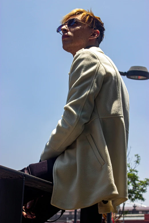 a man is walking along the street in a coat and sunglasses