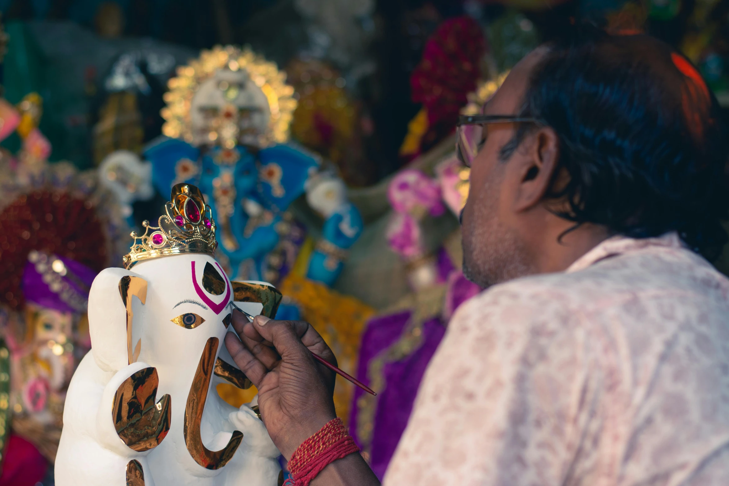 an older man decorating an ornately adorned ganesh idol