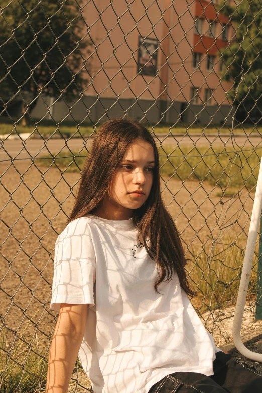 a girl sits on the ground near a fence