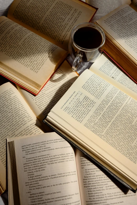 several open books, one containing some pages and a cup of coffee on a bed