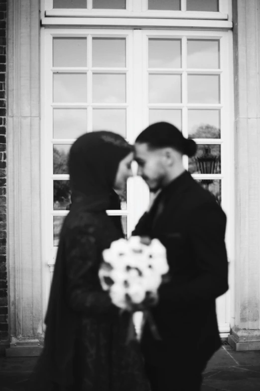 man in black outfit holding bouquet of flowers and woman in red coat facing the camera