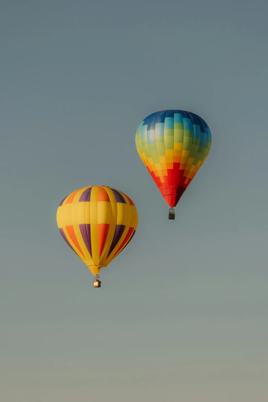 two  air balloons in the sky one with a multicolored design and one without with the same color