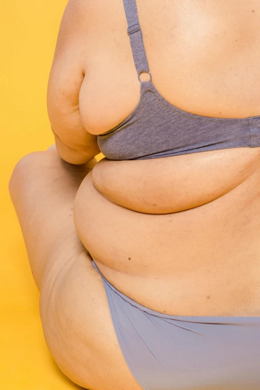a fat woman in a blue bikini sits down with her stomach in view