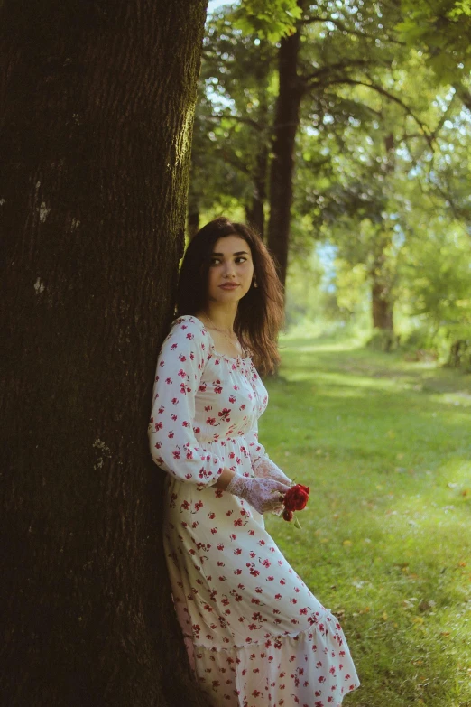 a woman leaning against a tree while wearing a white dress