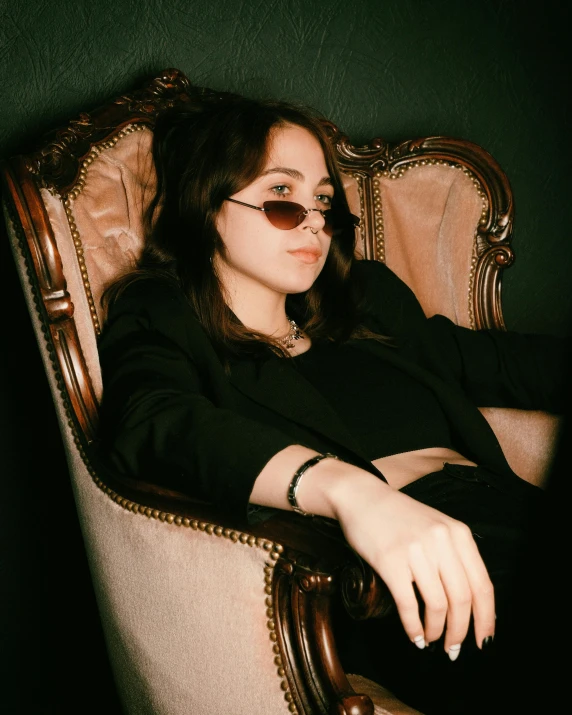 a woman sits in a chair wearing dark glasses