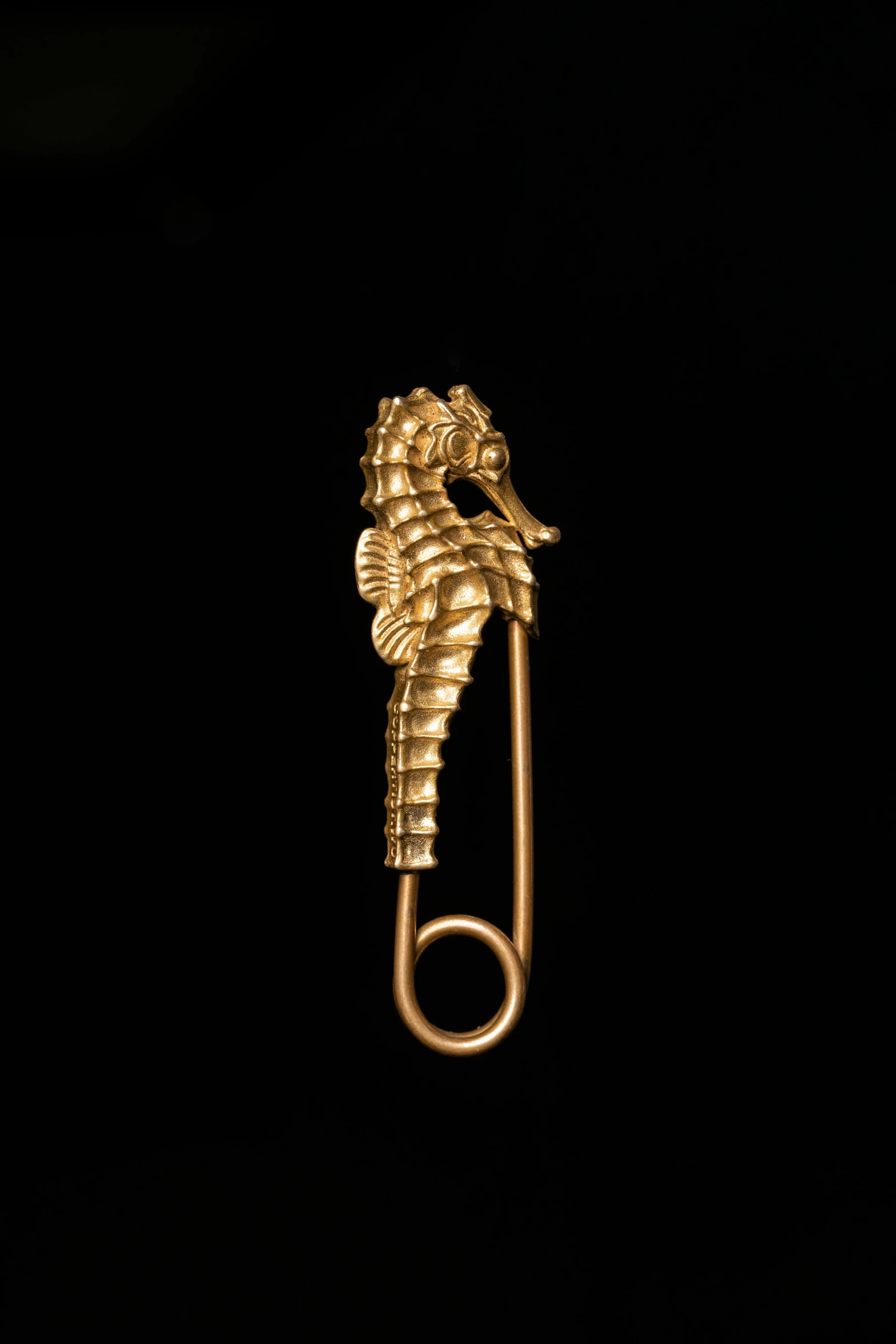 a yellow metal pin with a small seahorse sticking out of it