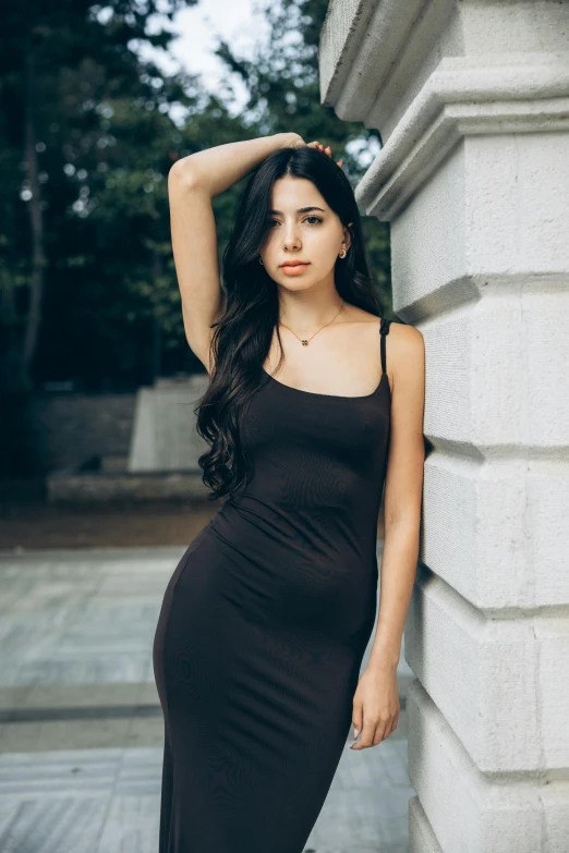 woman leaning on white column and wearing a black dress