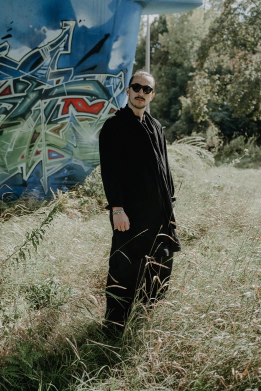 a man with sunglasses standing on the ground next to graffiti