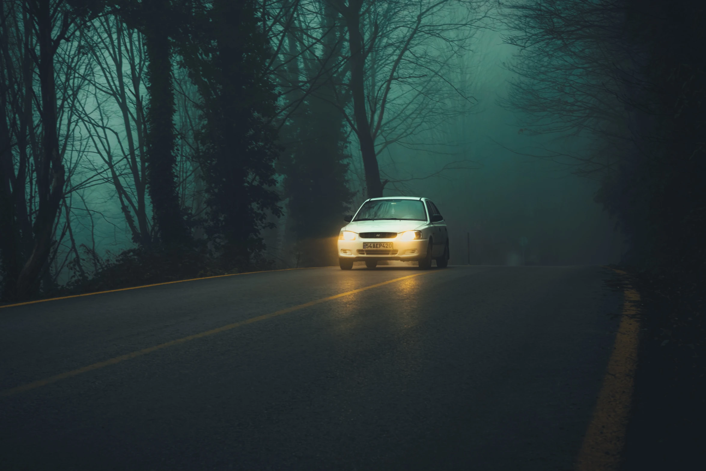 a car driving down the road on a foggy evening