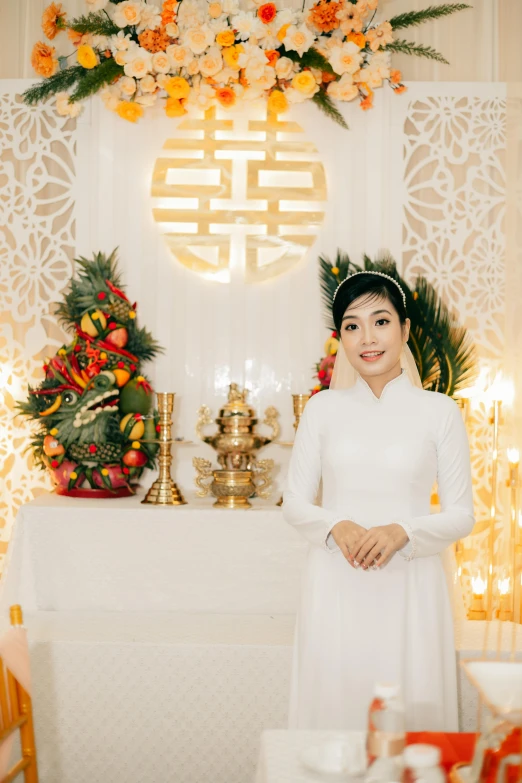 a young lady wearing a long white dress standing next to flowers