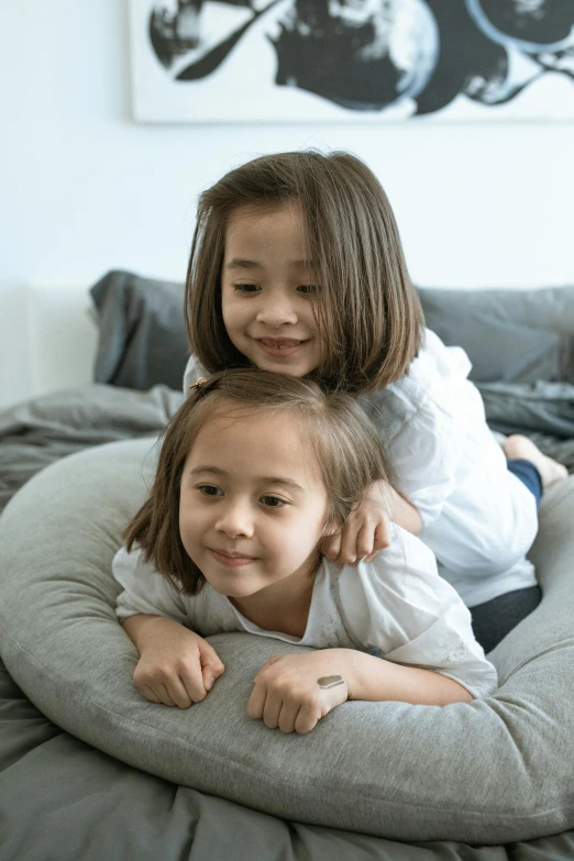 two little girls sit on top of a bed