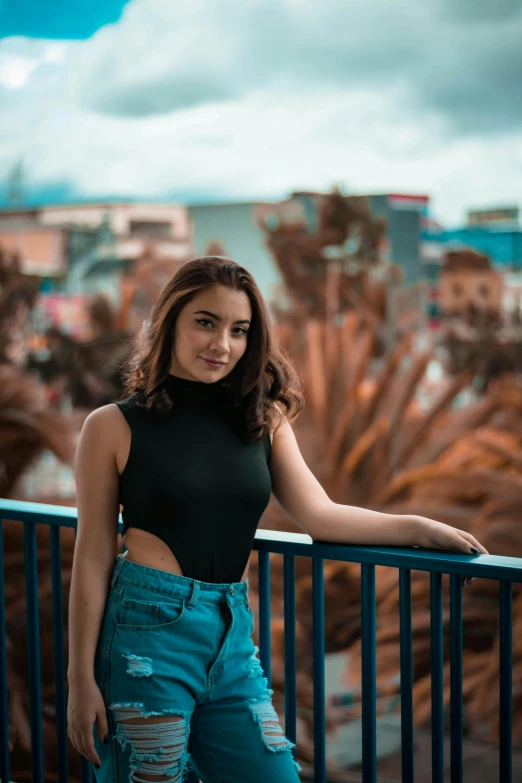 the woman in jeans stands next to a railing, with her arms on the rail