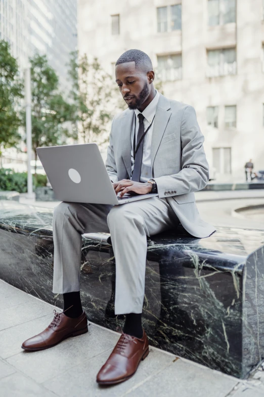 man in business attire sitting on a park bench using a laptop