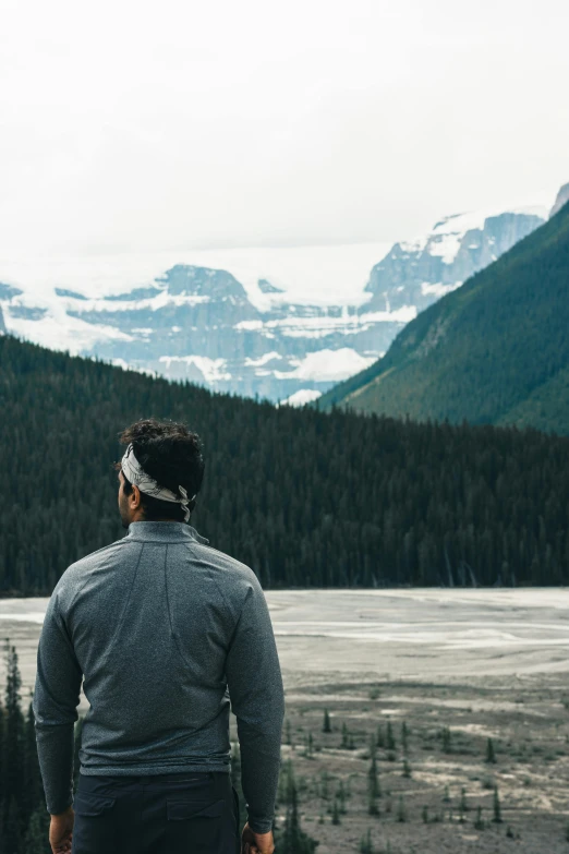 man standing with head band looking out on a snow covered mountain range