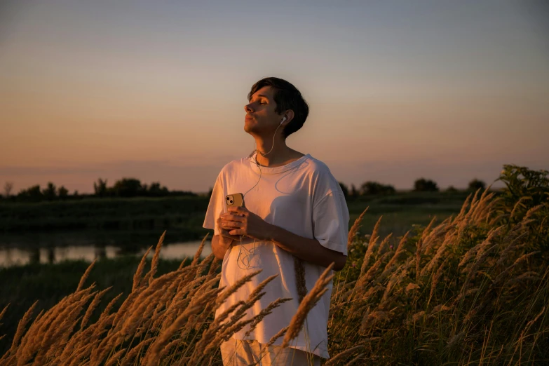 a young man stands among the tall grass looking at the sun