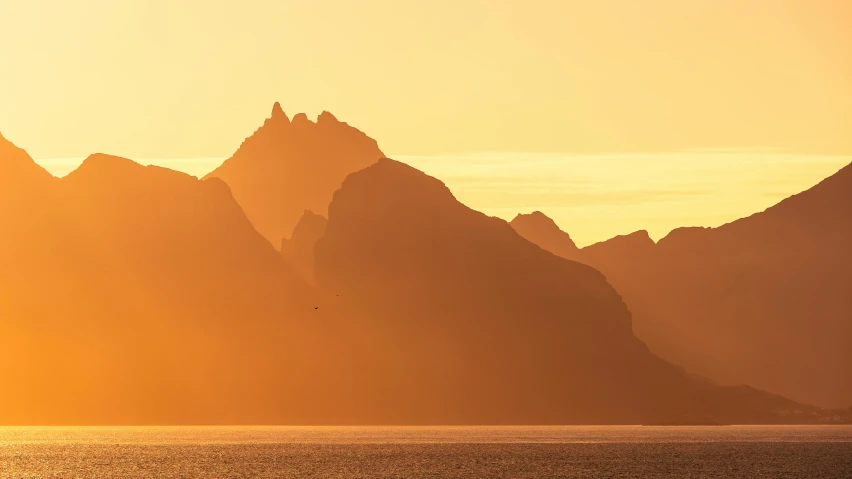 the setting sun reflects in the water as a large mountain range is shown behind the horizon