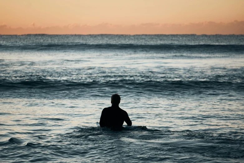 man sits on his surfboard in the ocean waiting for a wave
