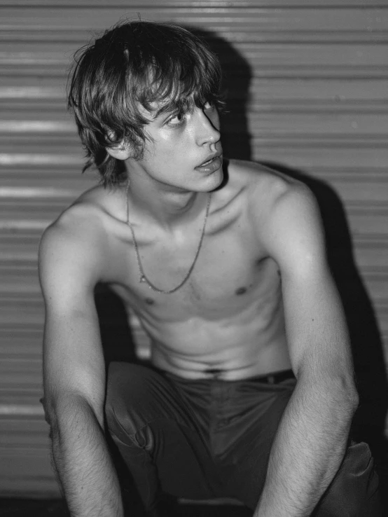 a man sitting next to a wall wearing a necklace