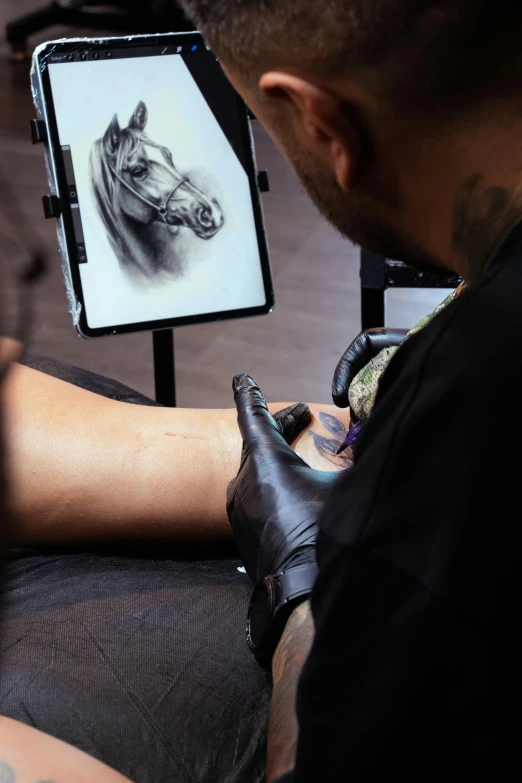 a man getting a tattoo done on his arm and a horse head behind him