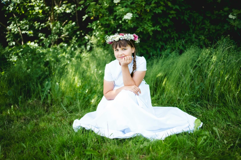 a  sits on a lawn while holding her chin