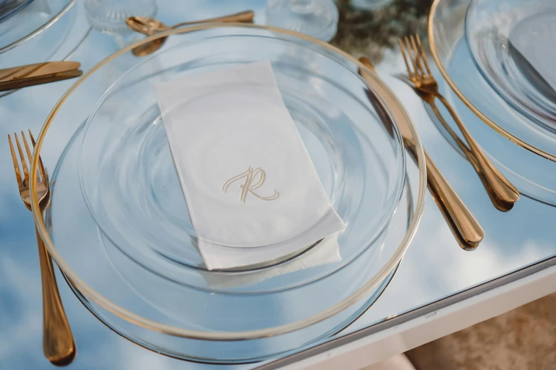 there is a clear glass table with gold plates and goldware