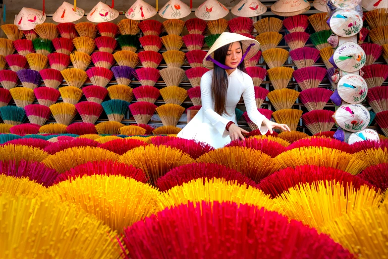 woman in white dress walking in front of colorful array of vases