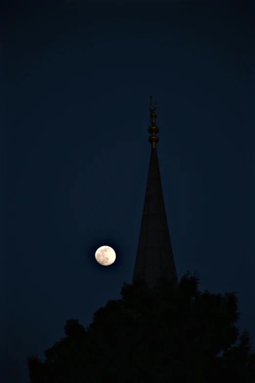 a full moon seen over the tops of some tall buildings