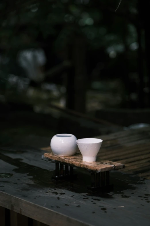 two white bowls sit atop the top of a wood surface