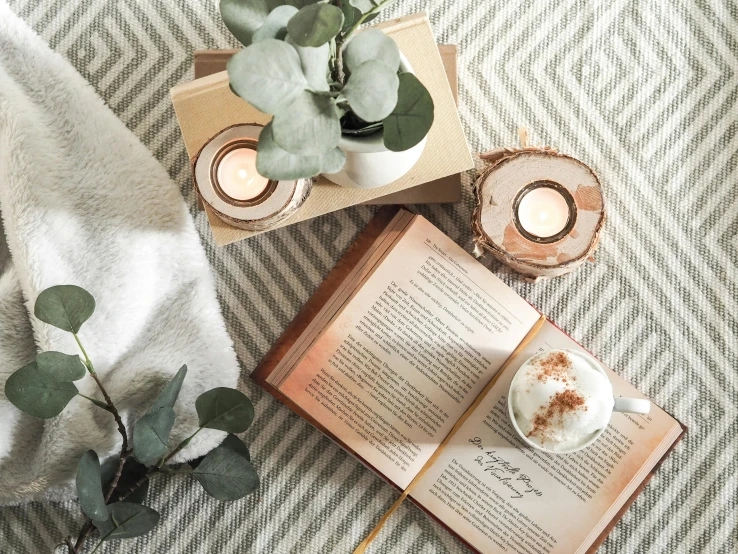 an open book with tea light candles, leaves and a pot of plant sit on top of a bed