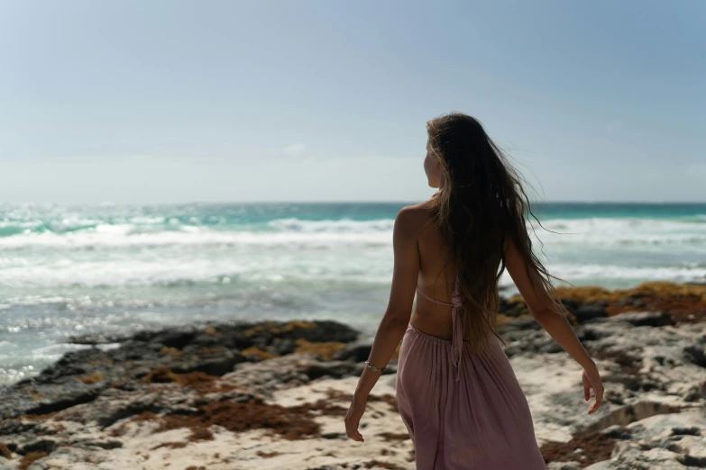 woman walking down beach, back to camera, with open water, ocean in background