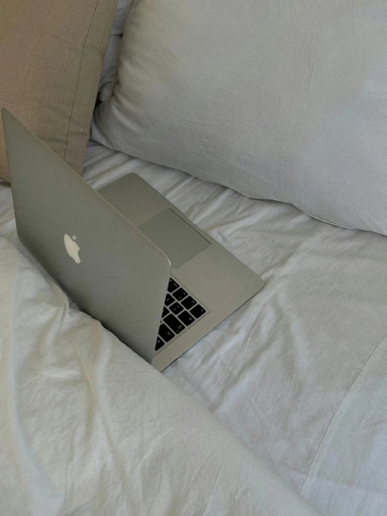 an apple laptop on the bed with the same side turned down