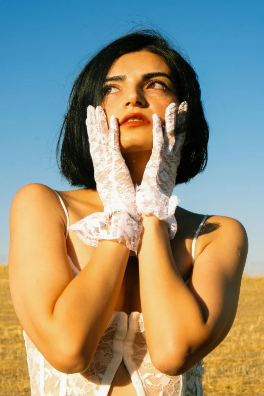 a woman in white lace gloves covers her eyes