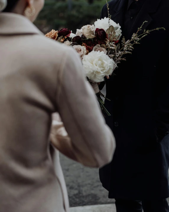 a man is standing with his arms behind a woman and holding a bouquet