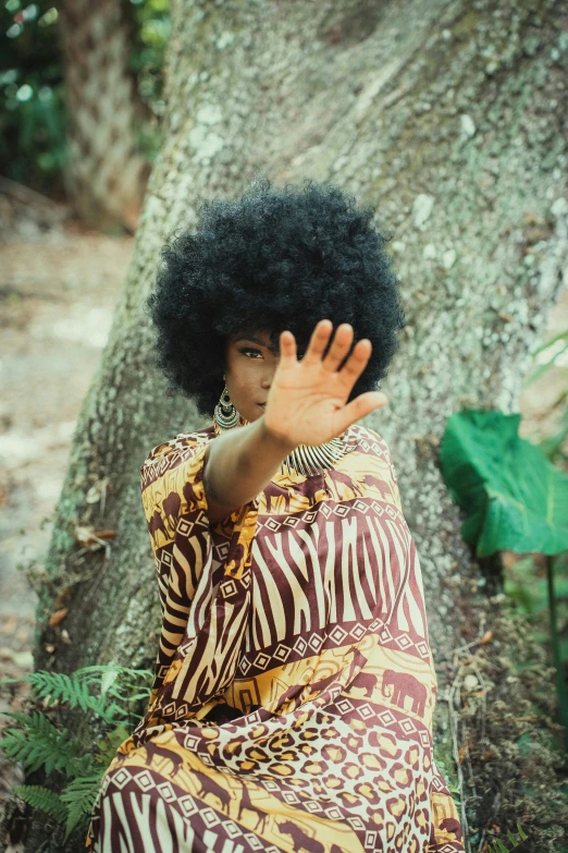 an older woman with a large afro is sitting on the ground in front of a tree