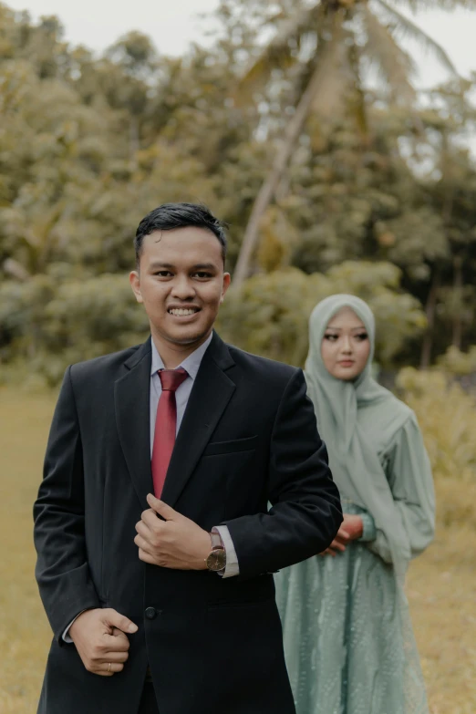 a man wearing a red tie in a grassy field next to another woman