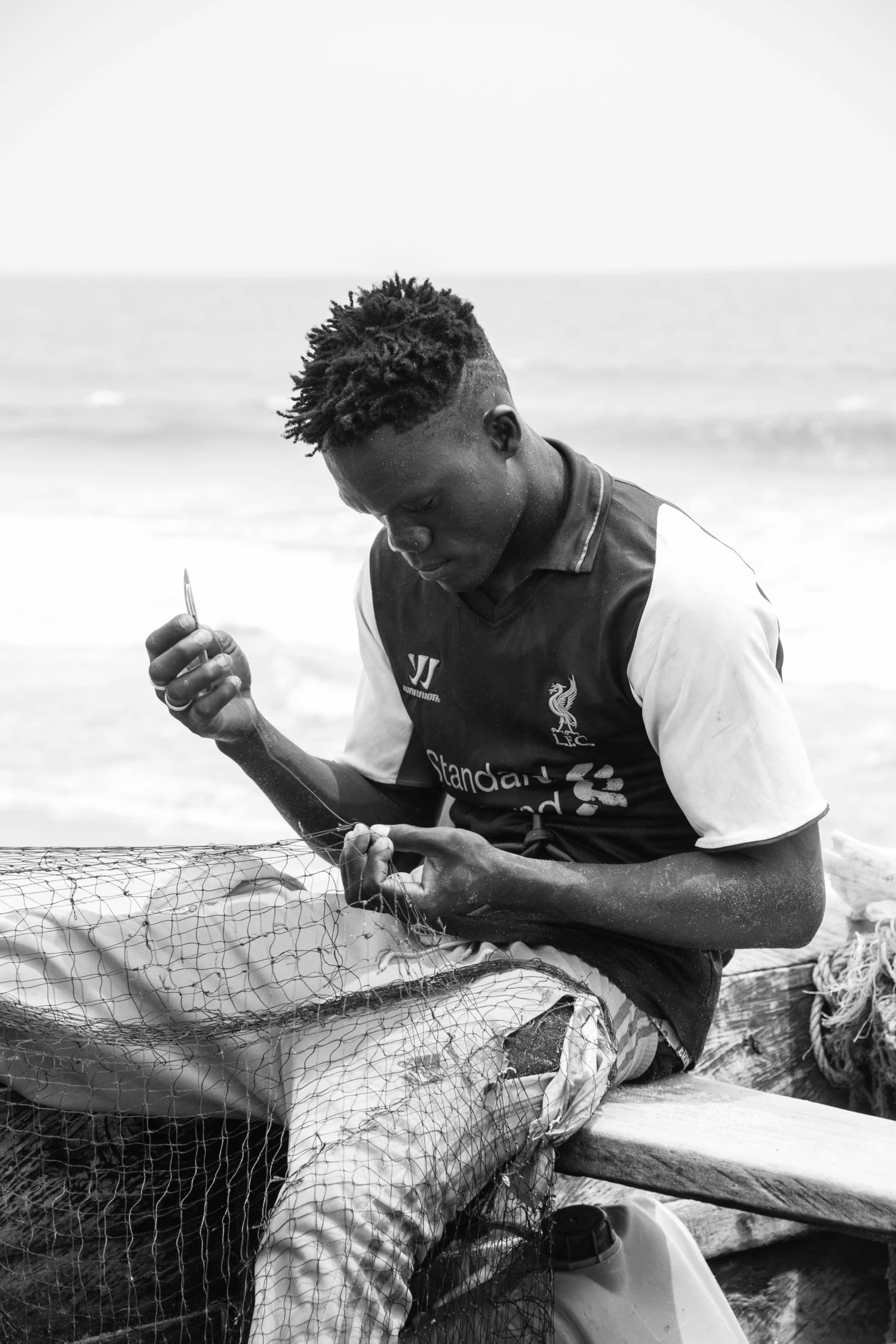 a man sits by the water, texting on his cell phone