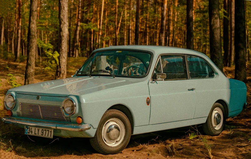an old blue car sitting in a clearing with trees