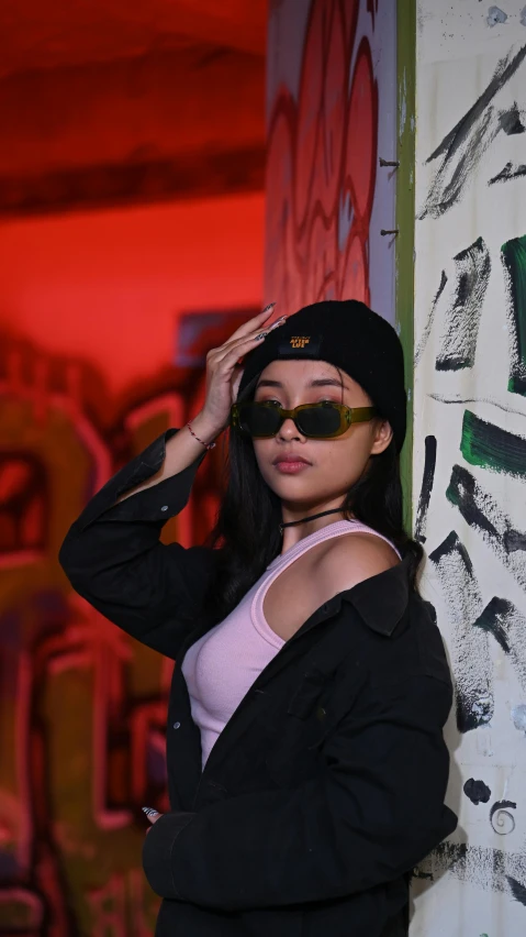 a woman in a beanie and sunglasses leaning against a wall