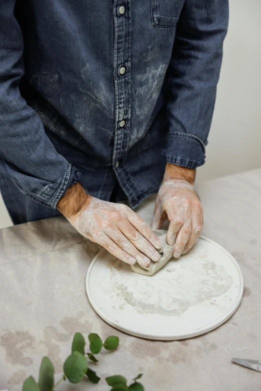 a person in black shirt and gloves kneading dough on a white table