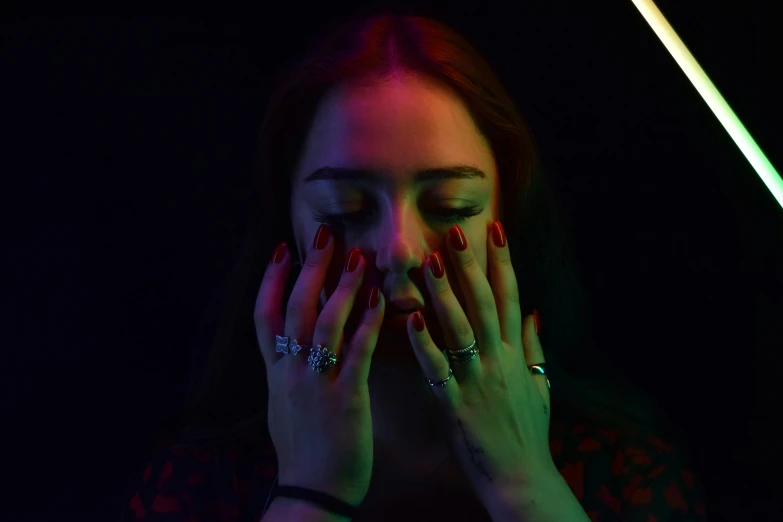 woman covering her face with hands, wearing dark lighting